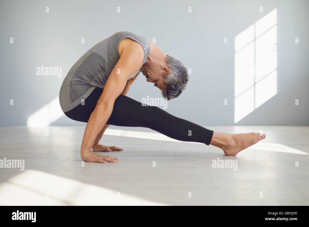 Yoga-Mann. Ein Mann übt Yoga-Balance in einem grauen Raum. Stockfoto