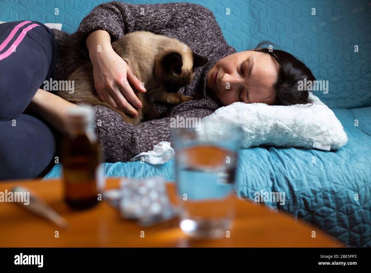Frau fühlt sich krank auf der Couch sitzend mit ihrer Katze in den Armen. Konzentriere dich auf das Gesicht der Frau. Stockfoto