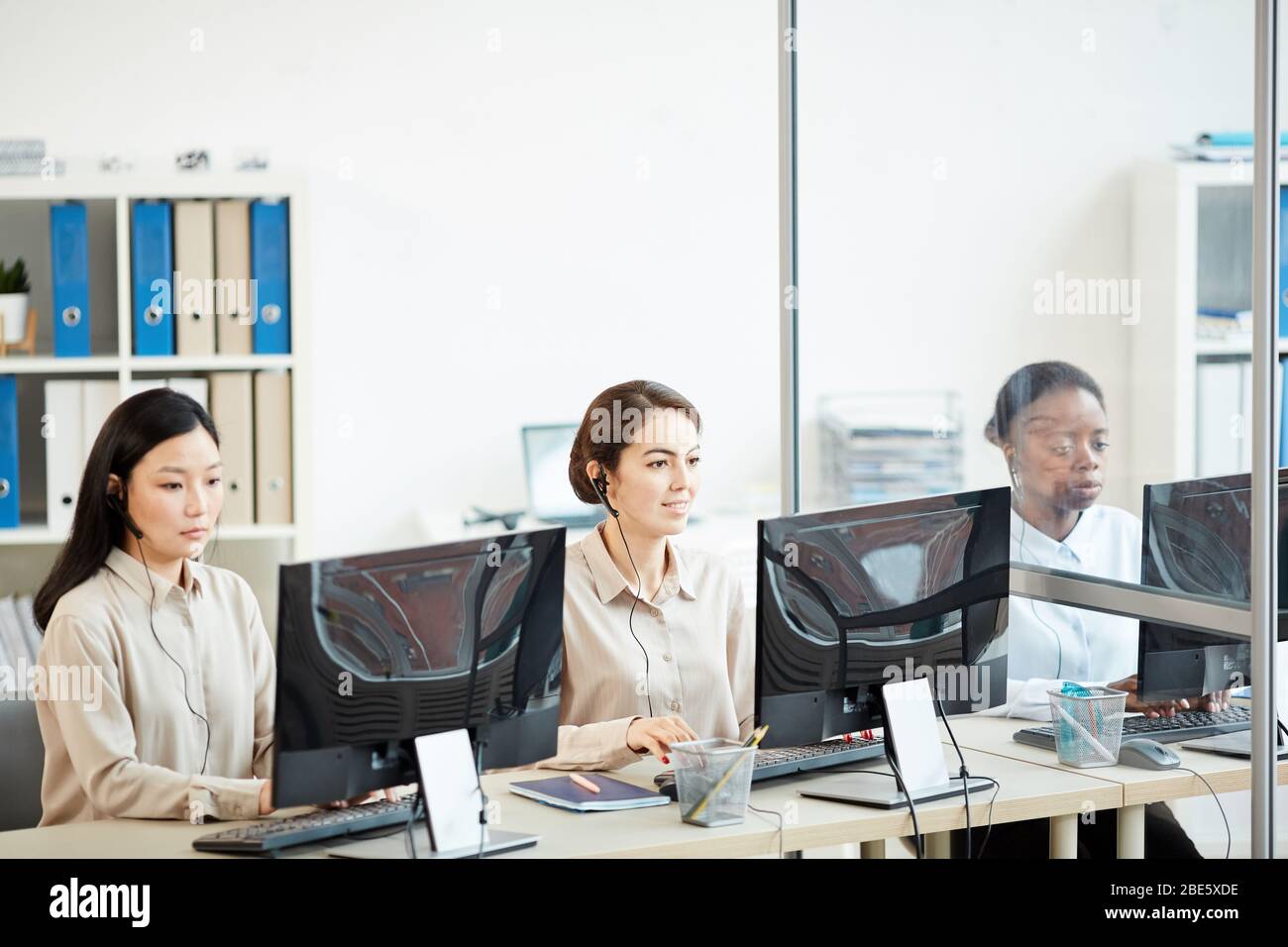 Porträt von drei weiblichen Bedienerinnen, die in Reihe sitzen und Computer im Callcenter-Büro nutzen, Kopierraum Stockfoto