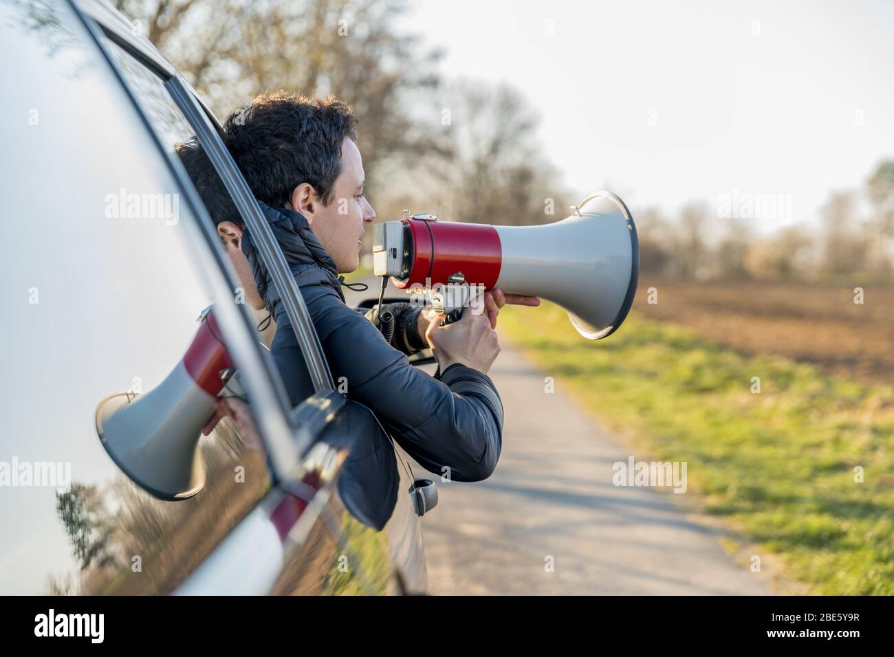Ein junger Mann brachte wichtige Nachrichten durch ein Autofenster in das Megaphon Stockfoto