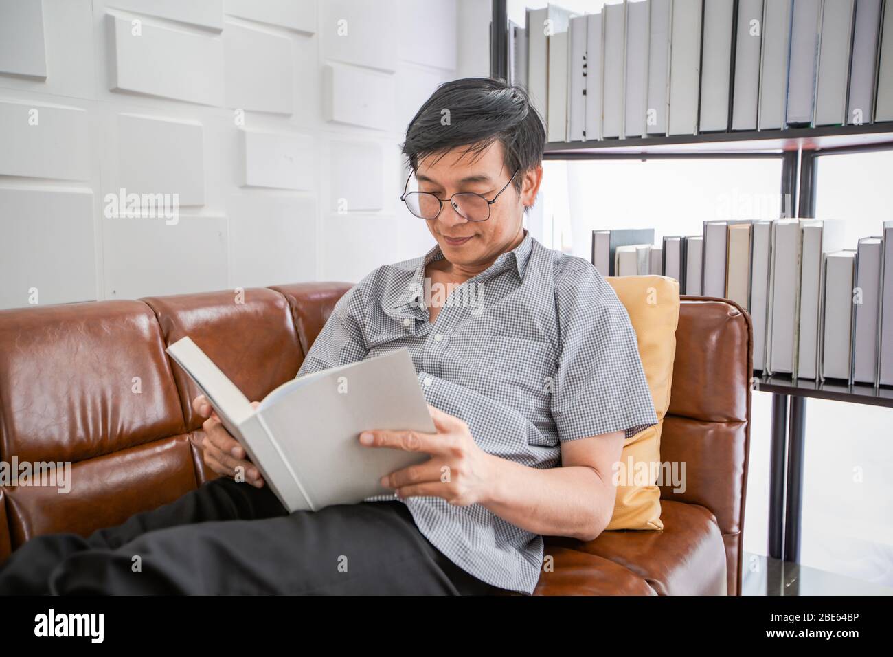 Senior Asian Mann Lesen Buch auf Sofa im Wohnzimmer zu Hause, Porträt von asiatischen älteren Mann ist entspannend und Glück mit Lesen Sie ein Magazin zu Hause Stockfoto