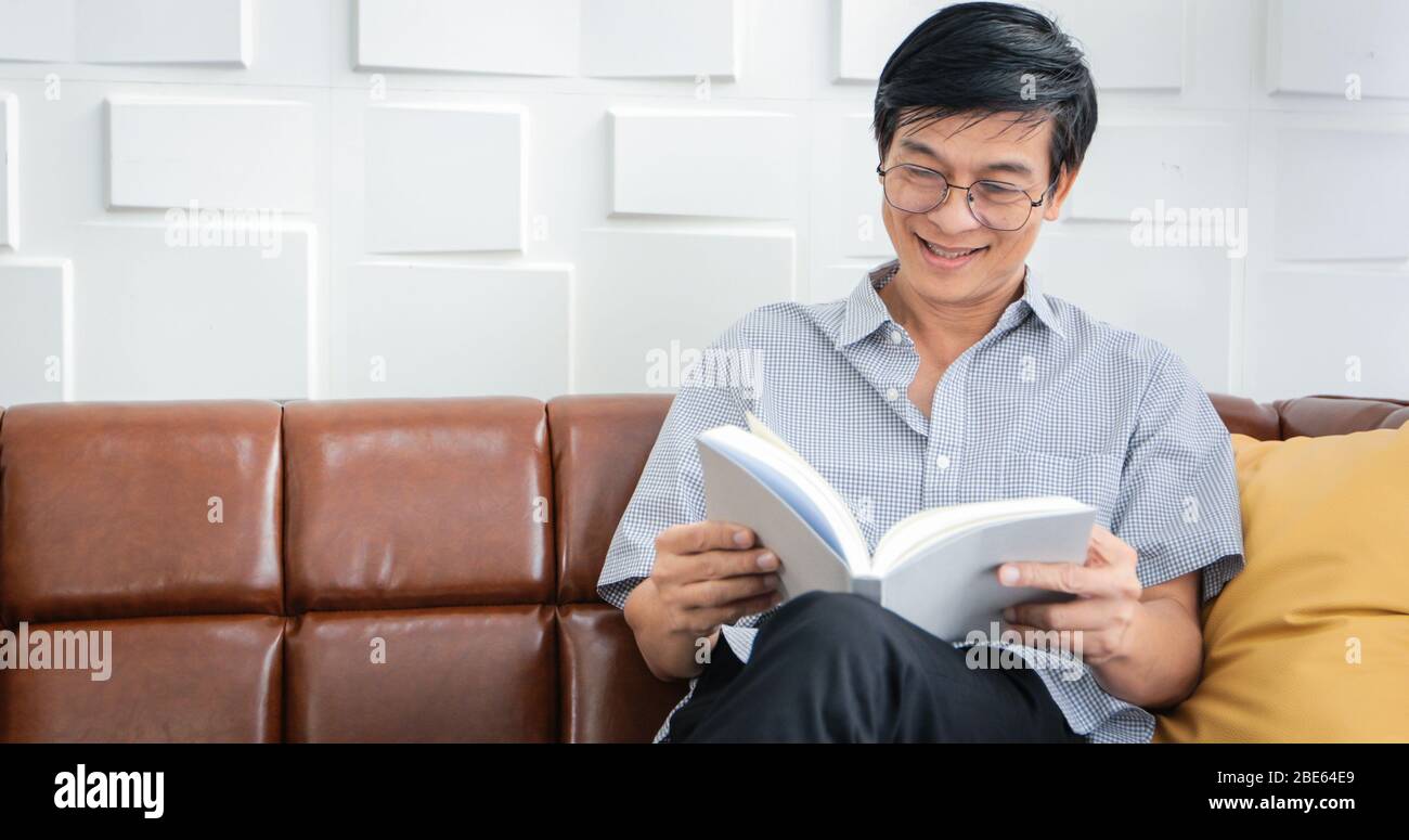Senior Asian Mann Lesen Buch auf Sofa im Wohnzimmer zu Hause, Porträt von asiatischen älteren Mann ist entspannend und Glück mit Lesen Sie ein Magazin zu Hause Stockfoto