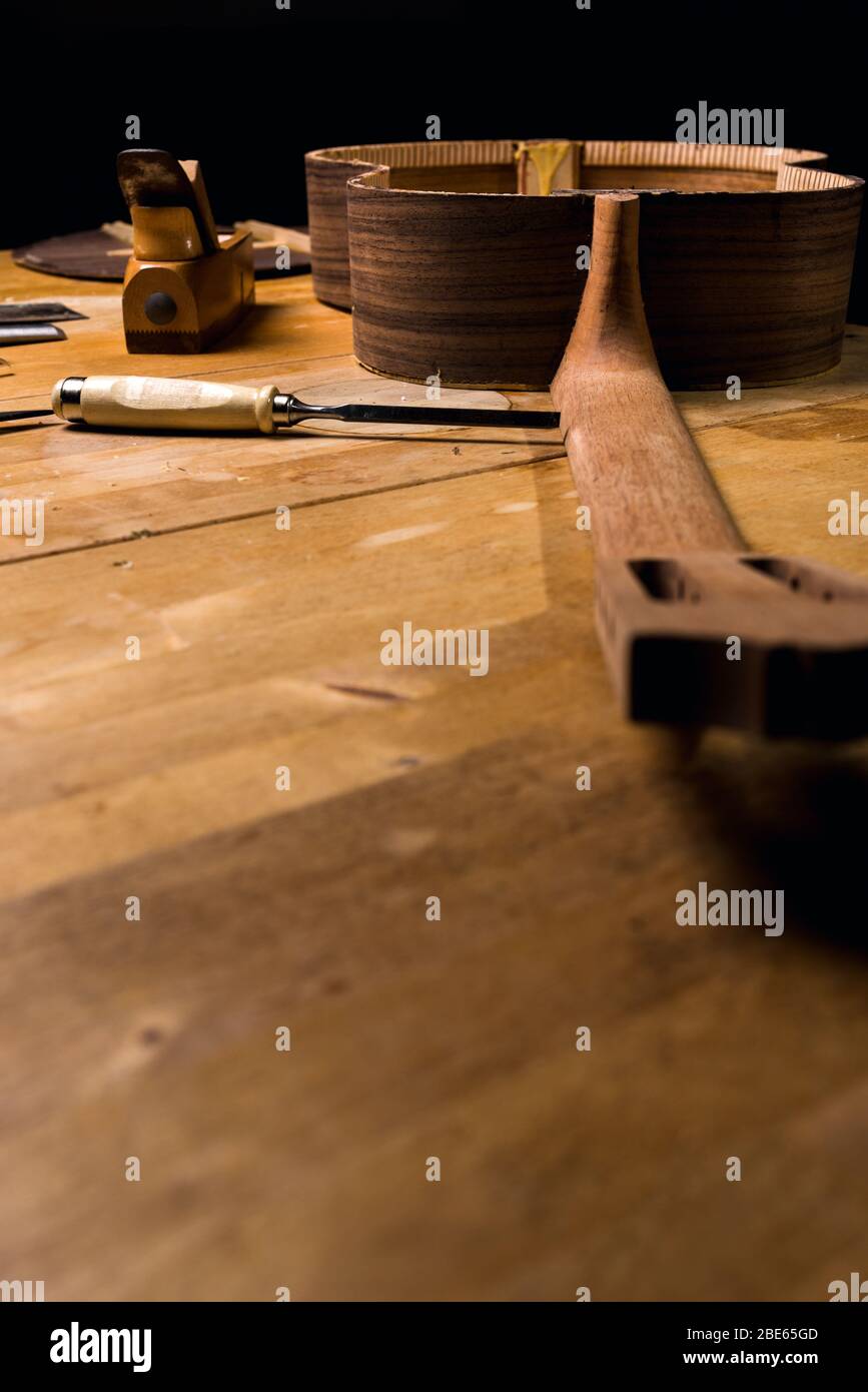Stillleben der Werkstatt luthería. Tisch mit Holz und Werkzeugen. Aushobel, Hobel. Vertikaler dunkelschwarzer Hintergrund. Stockfoto