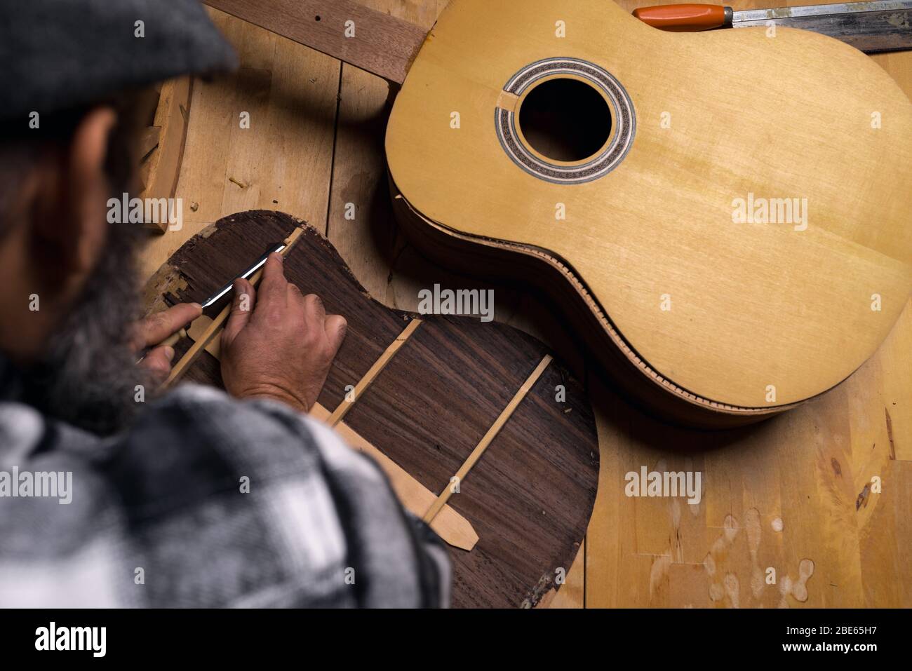 Luftaufnahme des Werkstatttisches des Gitarrenbauers. Handwerker debattieren Holz von der Rückseite der klassischen Palisander-Gitarre mit Gouge. Dunkelschwarzer Hintergrund. Stockfoto