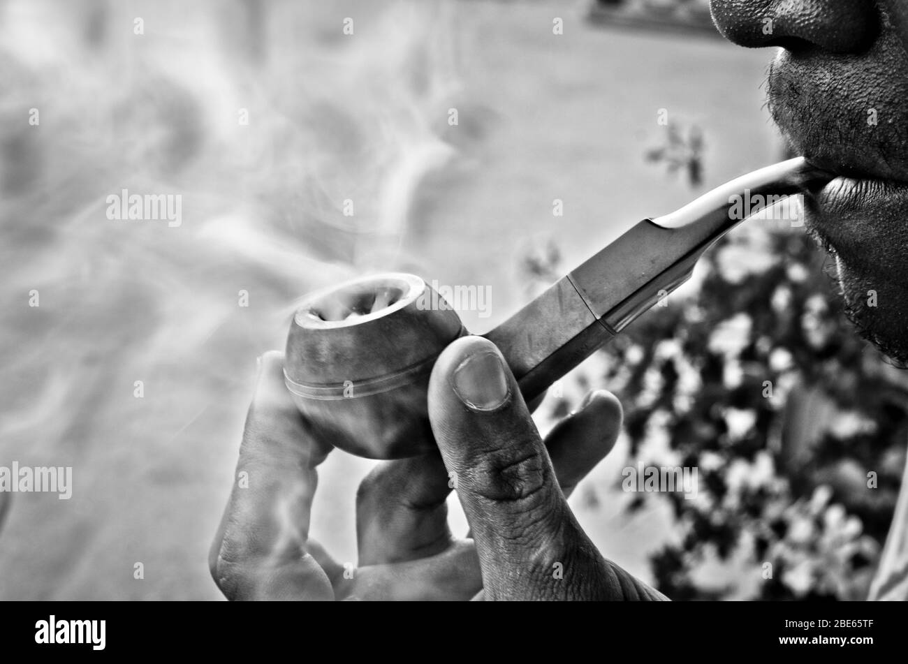 Fröhlicher junger Mann raucht mit Freude den Tabak in seiner Pfeife zwischen süßen Wirbeln und Rauchwolken Stockfoto