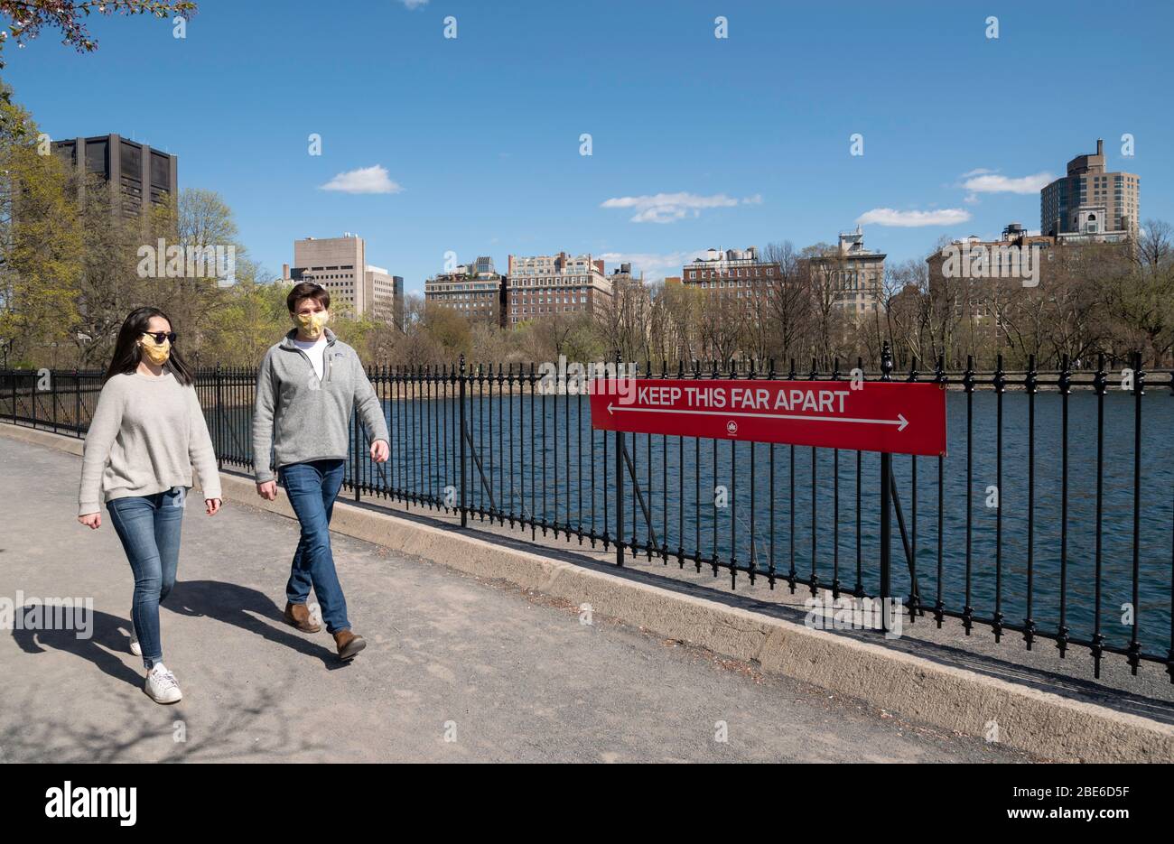 New York, NY, USA. 11. April 2020. Ein Paar in Schutzmasken geht an einem sozialen Distanzzeichen auf der Laufstrecke am Stausee in Central Par vorbei Stockfoto