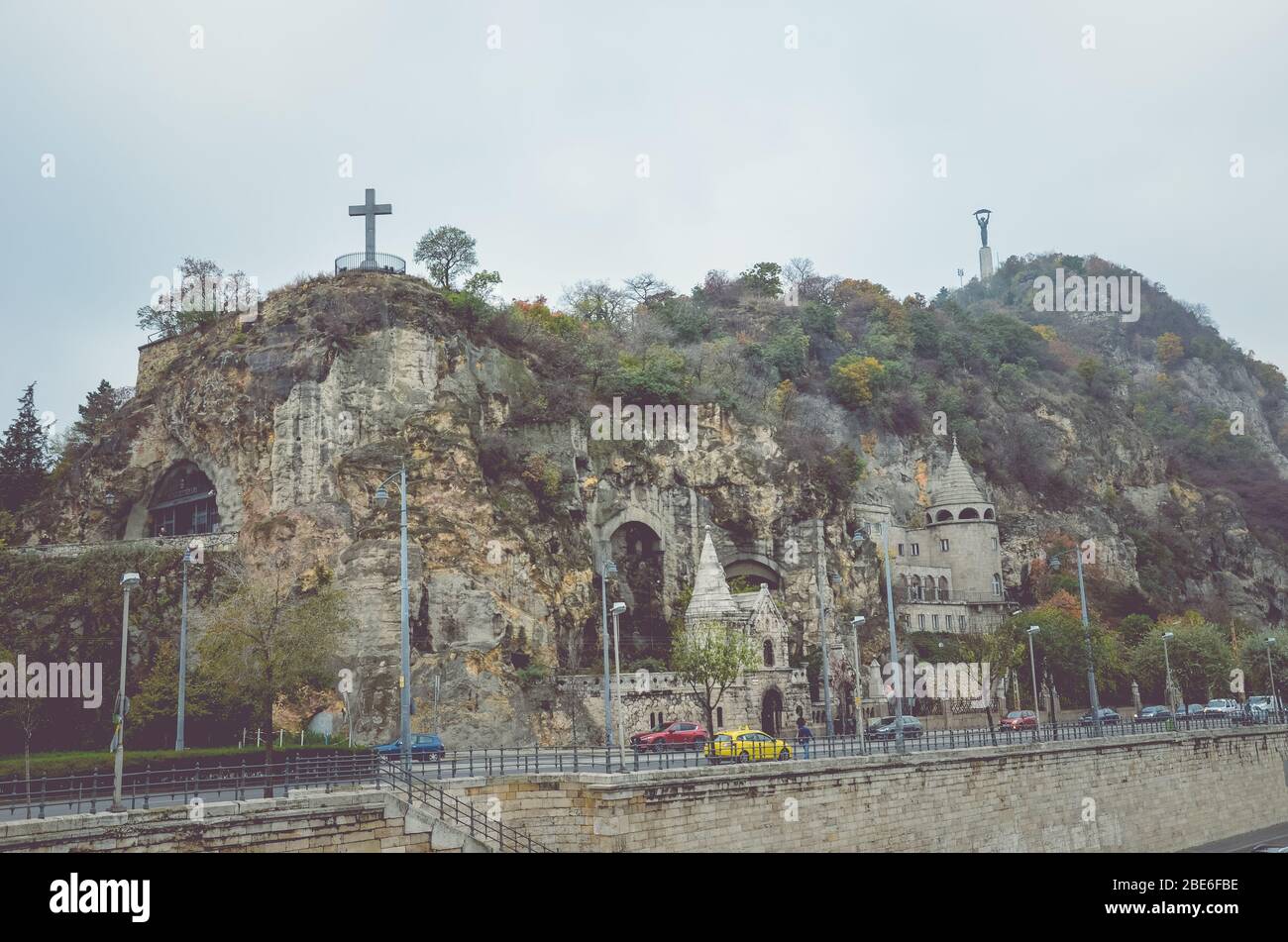 Budapest, Ungarn - 6. November 2019: Gellert Hill Cave Church, Sziklatemplom. Freiheitsstatue auf dem Hügel. Autos auf der Straße vor dem Hügel. Horizontales Foto. Ungarische Sehenswürdigkeiten. Stockfoto