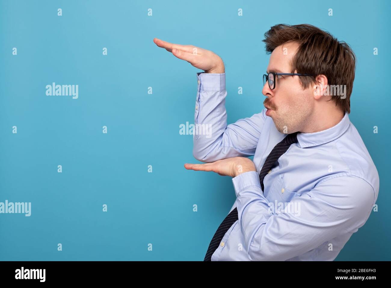 Lustig wütend schönen jungen Mann in blauem Hemd stehen in Karate Geste und bereit, anzugreifen. Innenaufnahme des Studios, isoliert auf blauem Hintergrund Stockfoto