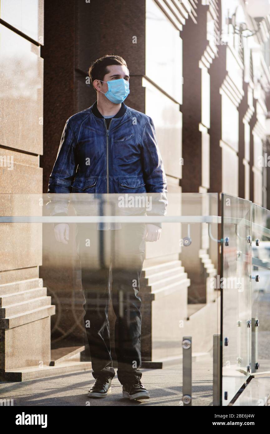 Porträt des jungen Mannes in schützender medizinischer Maske auf einem Hintergrund des modernen Gebäudes. Stockfoto