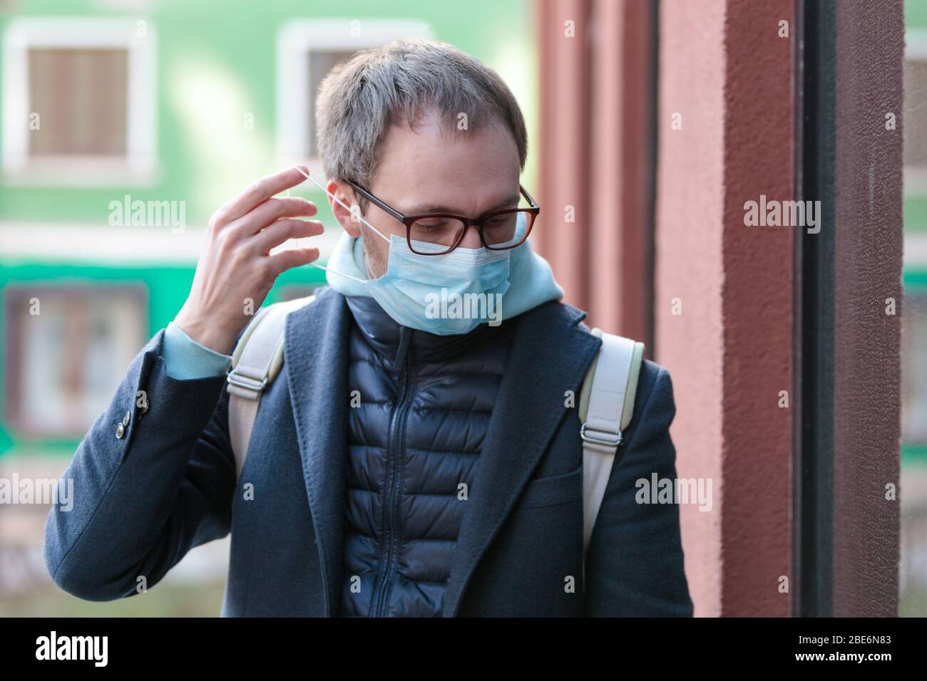 Kranker europäischer Mann in Brille trägt schützende medizinische Maske im Freien, Gebäude auf Hintergrund, Nahaufnahme. Grippeepidemie, Stauballergie, Schutz gegen Stockfoto