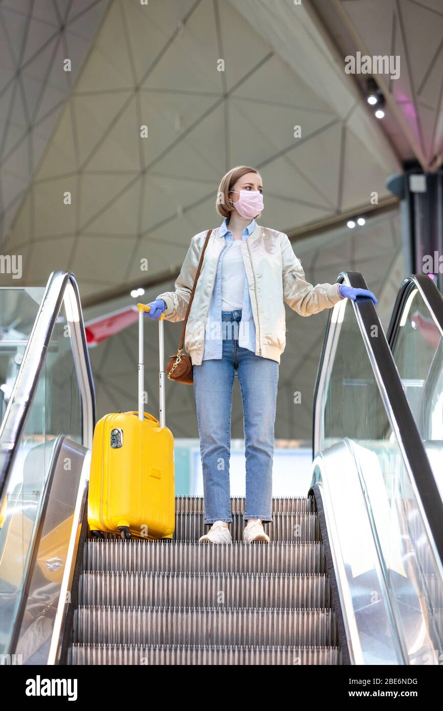Frau mit gelbem Gepäck steht auf der Rolltreppe am fast leeren Flughafenterminal wegen der Reisebeschränkungen für Coronavirus-Pandemie/Covid-19-Ausbruch. Stockfoto