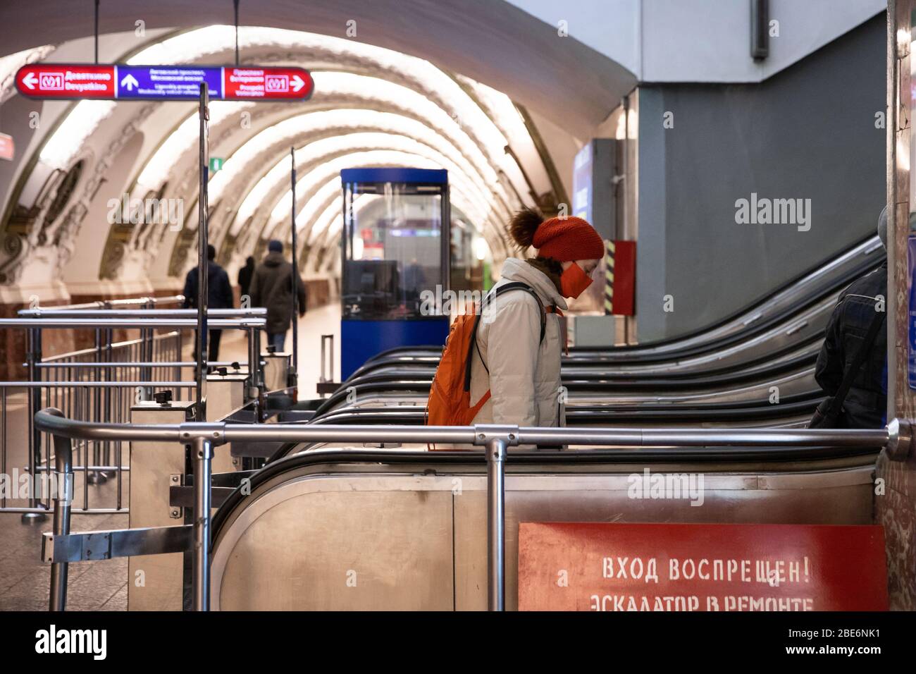 St. Petersburg, Russland - 05. April 2020. Frau Passagier trägt rote Schutzmaske steigt auf Rolltreppe.Fast leer Station der St. Petersburg U-Bahn d Stockfoto