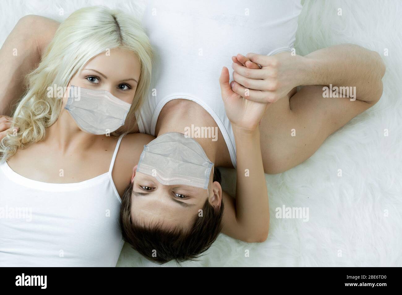 Hübsches Paar in medizinischer Maske, auf dem Boden liegen, Konzept Coronavirus Epidemie Stockfoto