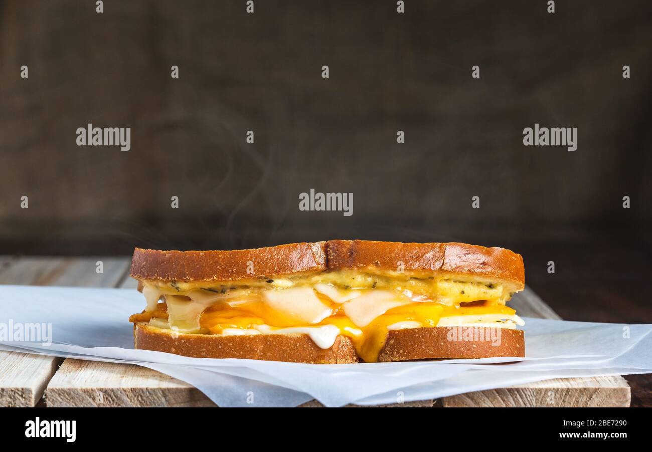 Gegrilltes Käsesandwich mit Dampf auf Metzgerpapier und Holzoberfläche Stockfoto