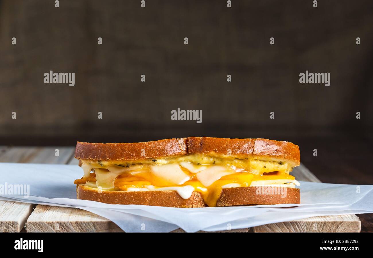 Gegrilltes Käsesandwich mit geschmolzenem Käse auf Fleischpapier auf Holzfläche Stockfoto