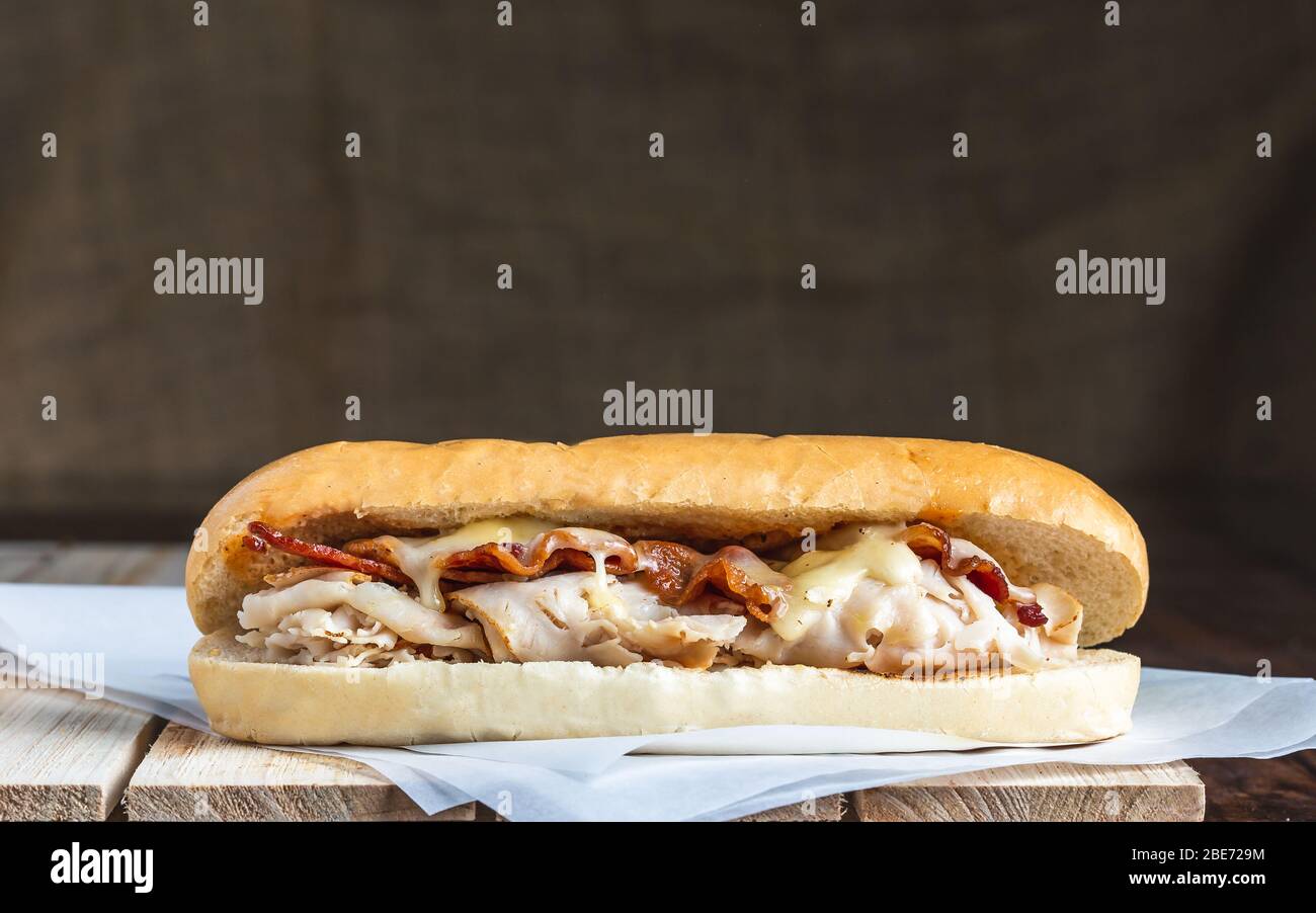 Bacon und pute Sandwich mit geschmolzenem Käse auf Metzgerpapier und Holzoberfläche Stockfoto