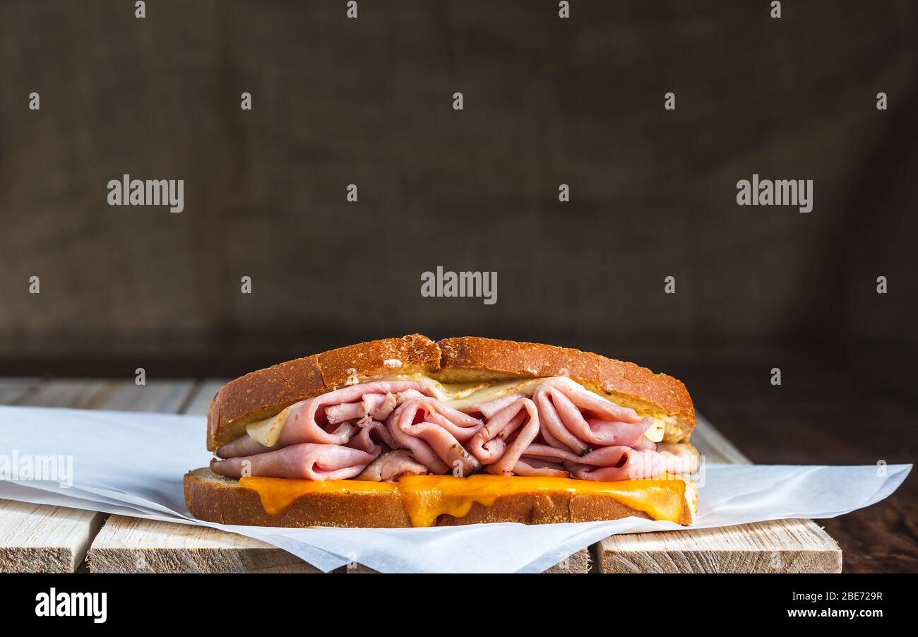 Sandwich mit Schinken und geschmolzenem Käse auf Fleischpapier und Holzoberfläche Stockfoto