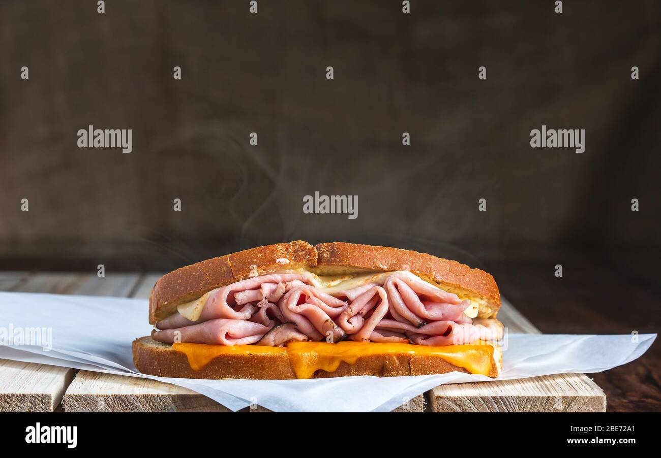 Sandwich mit Schinken und geschmolzenem Käse mit Dampf auf Fleischpapier und Holzoberfläche Stockfoto