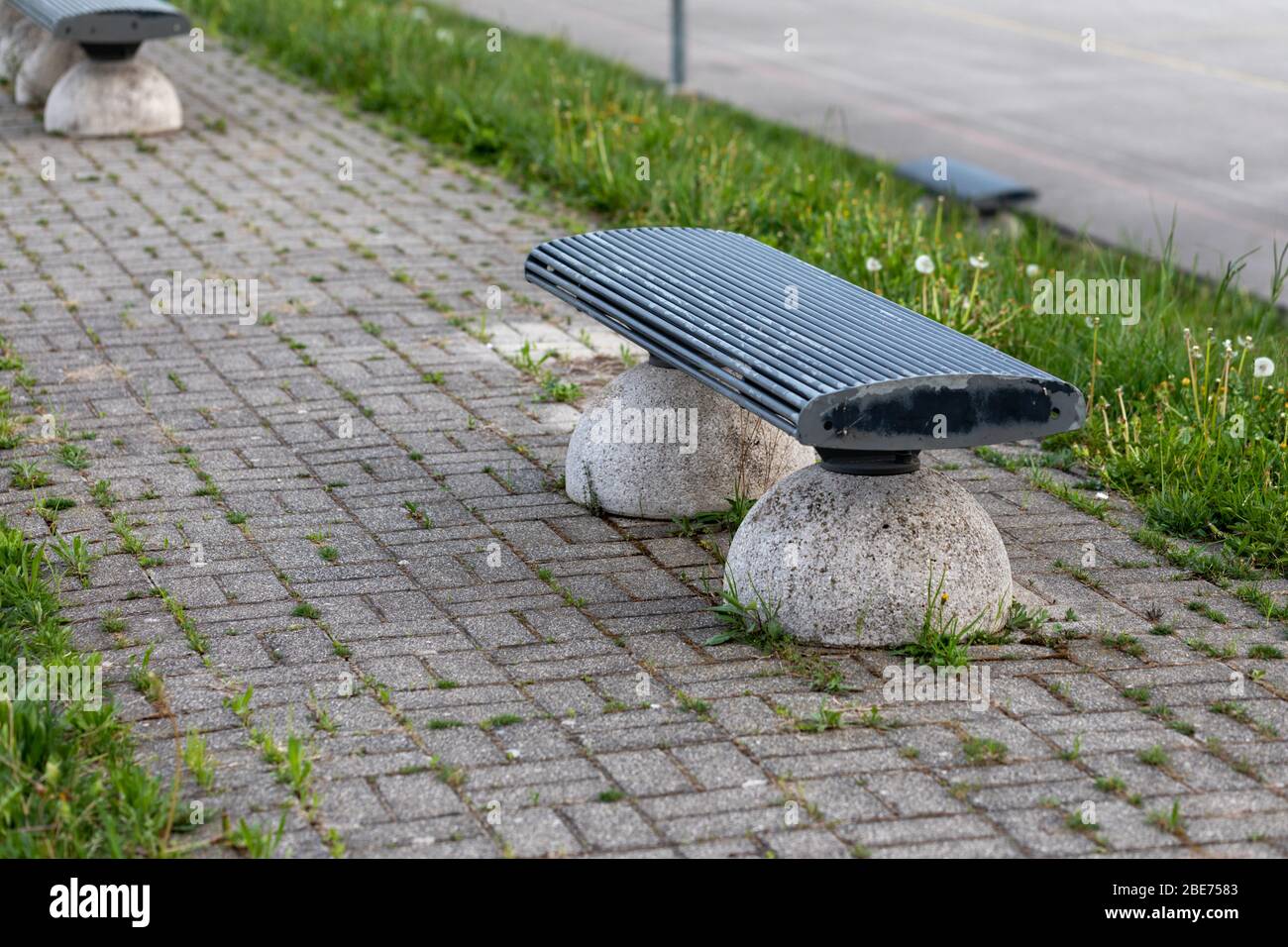 Leerstehende, menschenleere Parkbank mit ungeschnittenem Gras und Frühlingsblumen aufgrund der Sperrung des Coronavirus oder der Covid-19-Pandemie in einem konzeptionellen Bild Stockfoto
