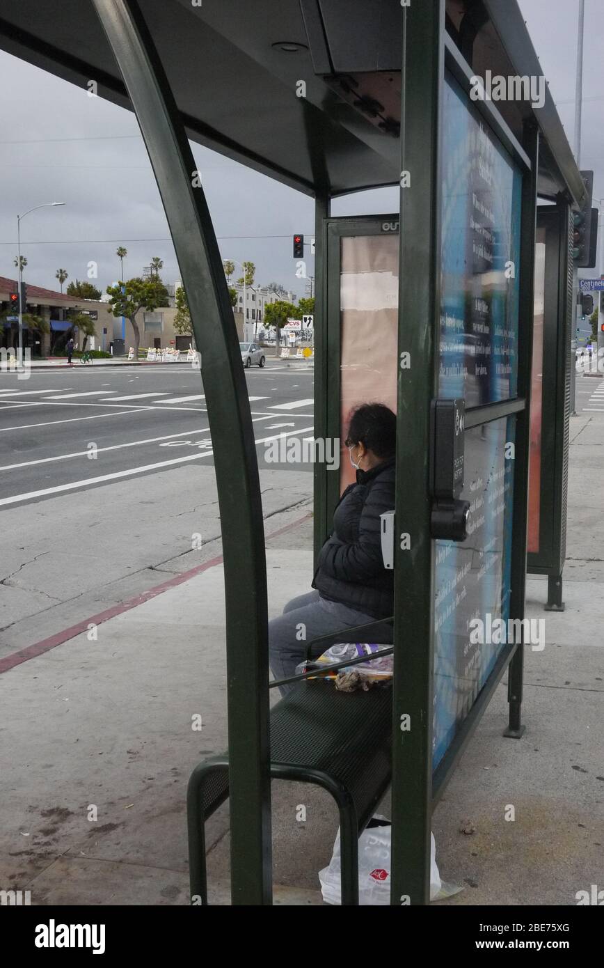Frau wartet an einer Bushaltestelle allein mit Schutzmaske. Stockfoto