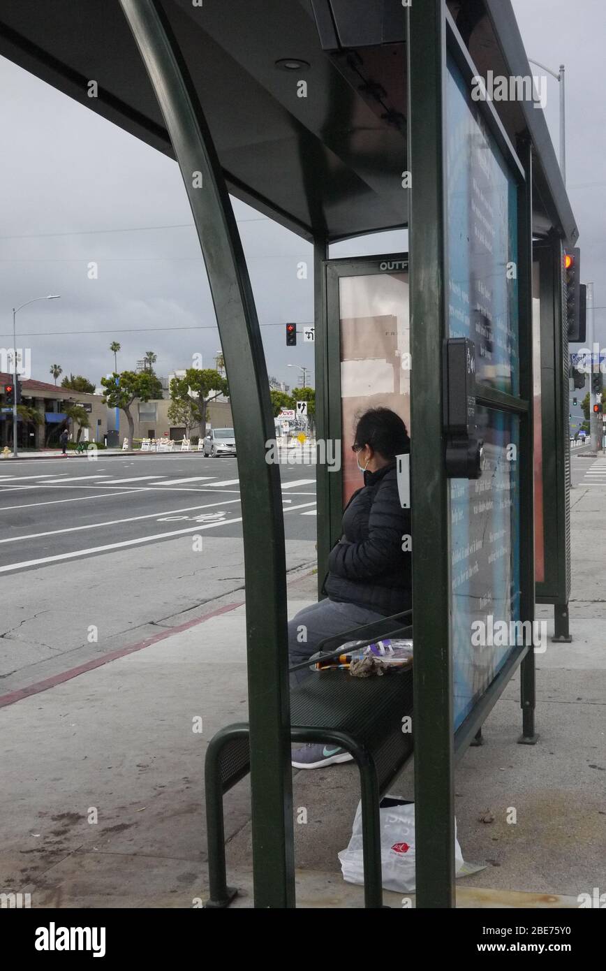 Frau wartet an einer Bushaltestelle allein mit Schutzmaske. Stockfoto