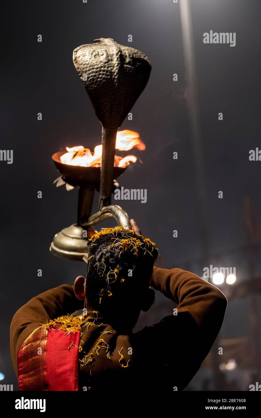 Junge Devotee Durchführung Aarti in Varanasi mit einer Cobra-förmigen Lampe mit brennenden Feuer und Blütenblätter auf seinem Haar Stockfoto