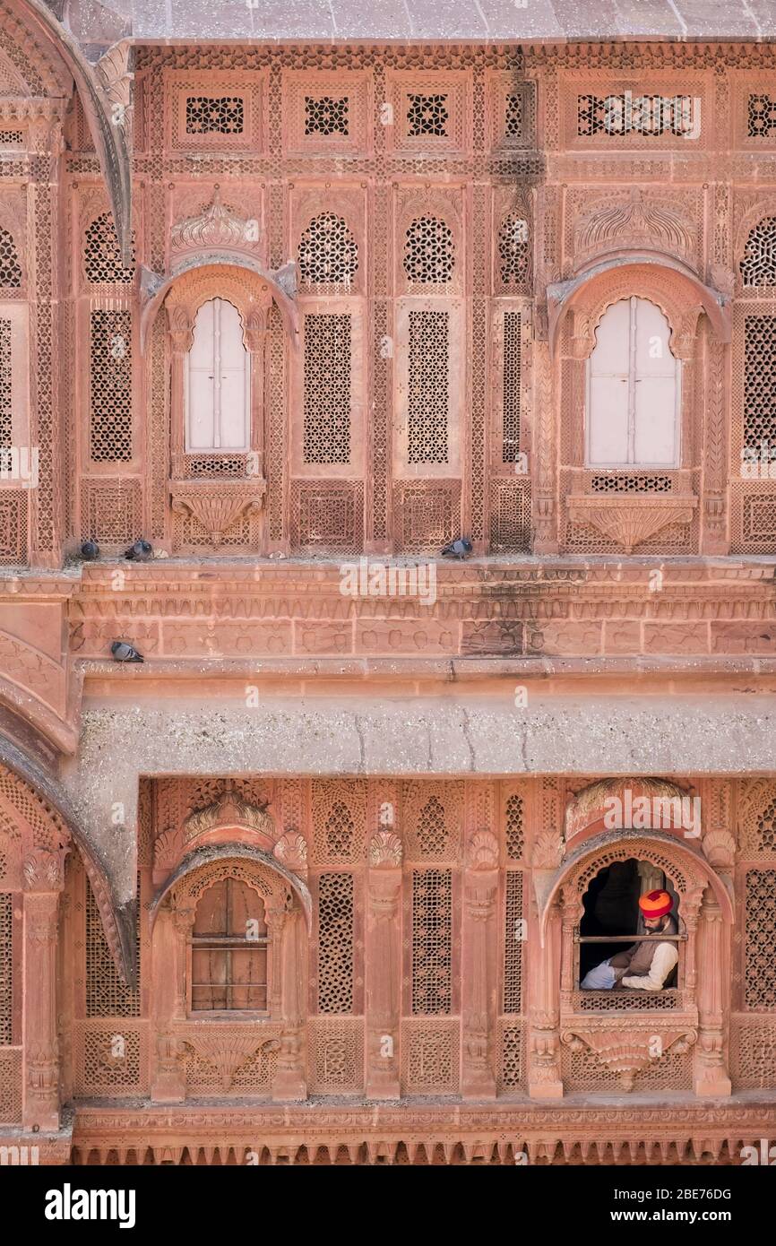 Ein Wächter in einem hellen, orangefarbenen Turban, der durch das Fenster von Mehrangarth schaut, einem großen, indischen Stein und aufwendig geschnitzten Fort Stockfoto