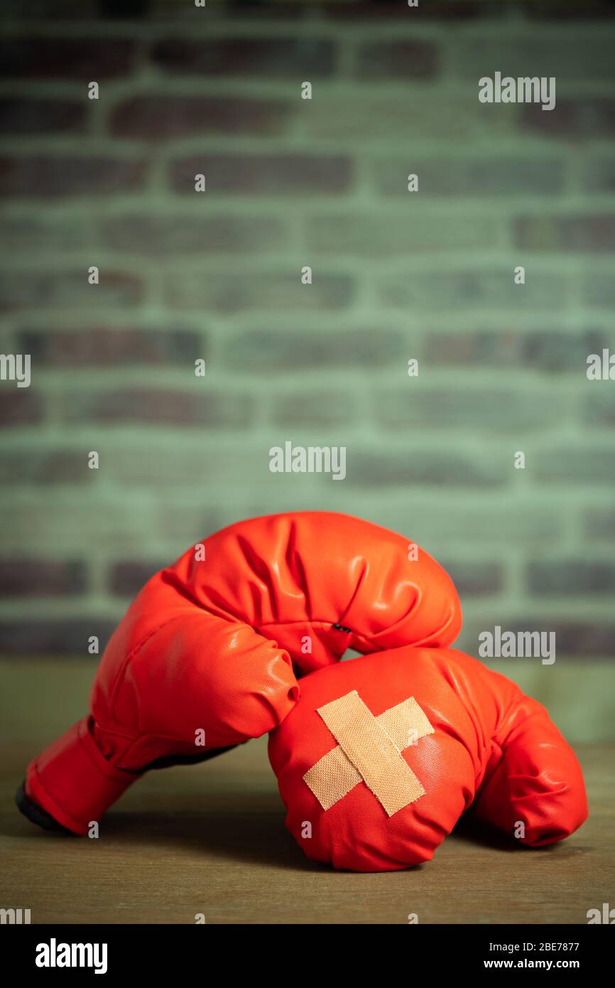 Rote Boxhandschuhe auf Holztisch und Ziegelwand in der Sporthalle. Kleberputz übereinander auf Boxhandschuhen. Idee, verletzt zu werden oder zu bekämpfen Stockfoto