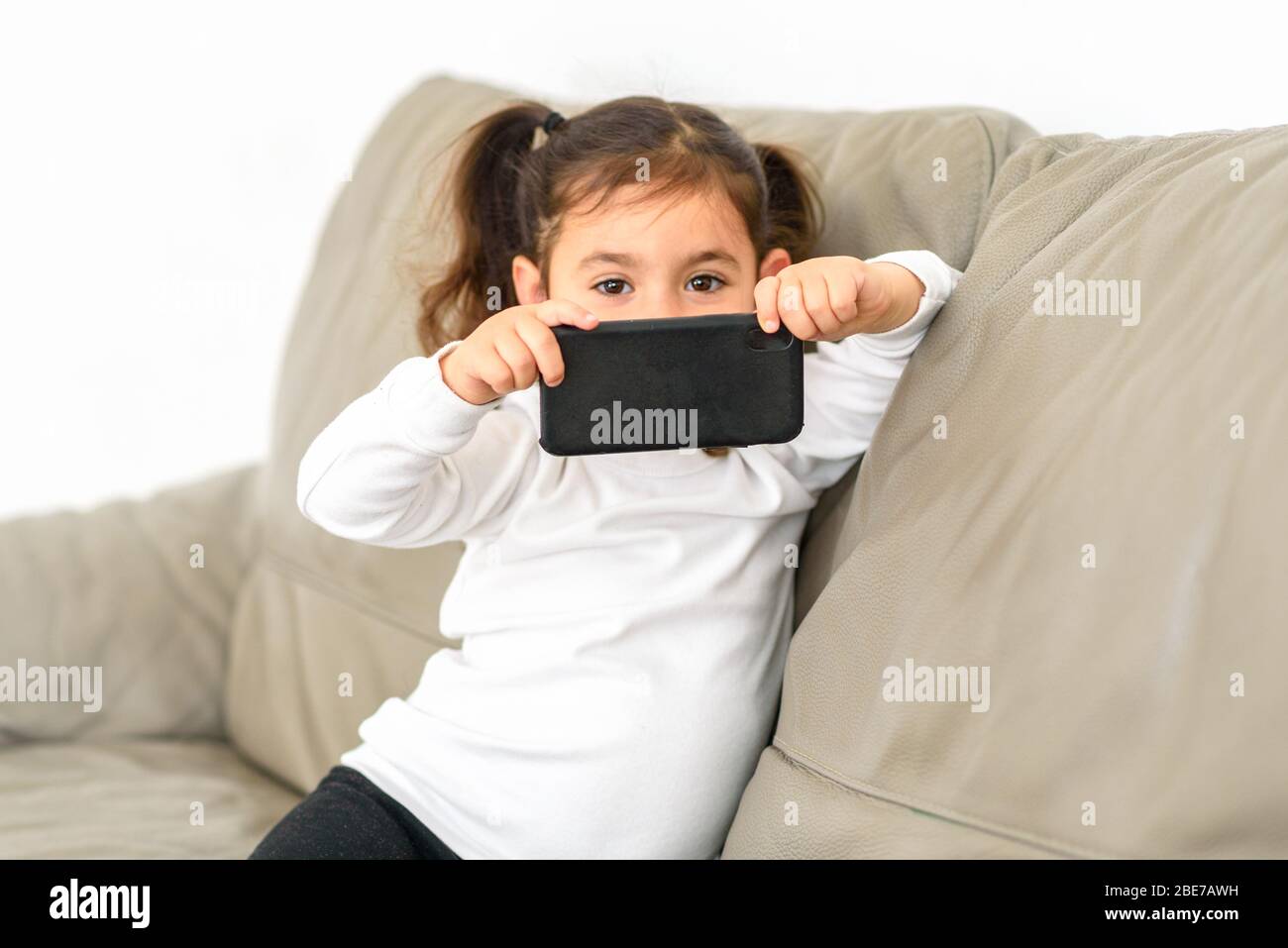 Kleines Mädchen, das Fotos auf einem Handy in der Wohnung. Stockfoto