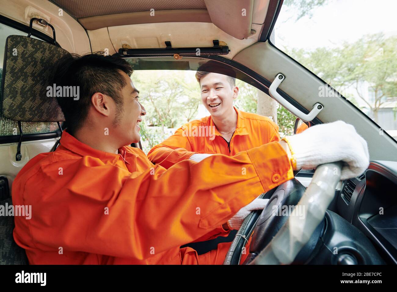 Lächelnde vietnamesische Lieferdienstfahrer in Uniform, die vor Beginn der Arbeit Smalltalk halten Stockfoto