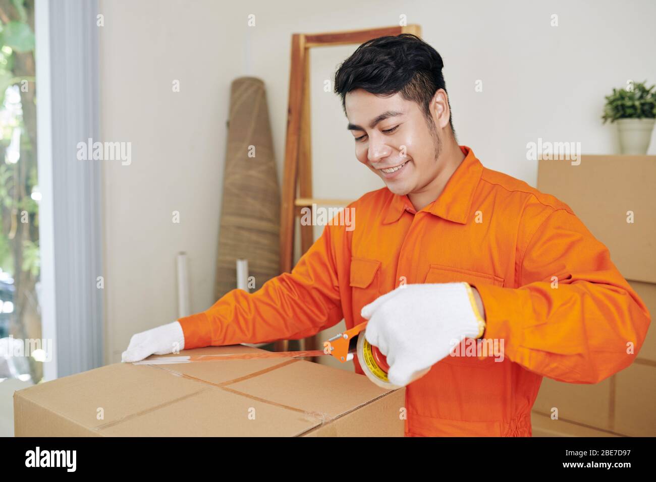 Lächelnd positiv Vietnamese Umzug Service Arbeiter mit Klebeband zu verschließen Kisten mit Habseligkeiten Stockfoto