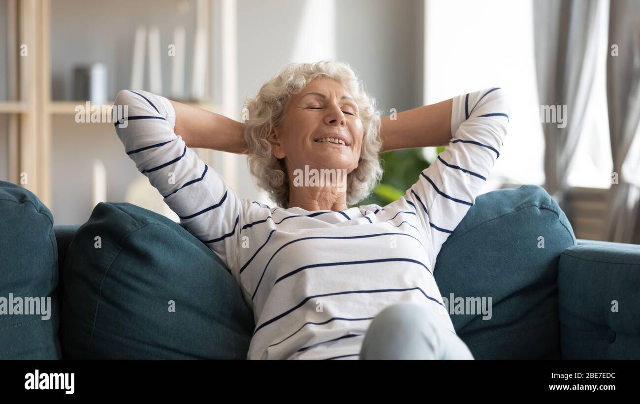 Lächelnde ältere Frau lehnt sich zurück, auf gemütlicher Couch entspannen Stockfoto