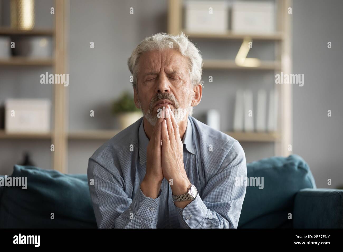 Trauriger älterer Mann mit geschlossenen Augen, der mit Hoffnung betet Stockfoto