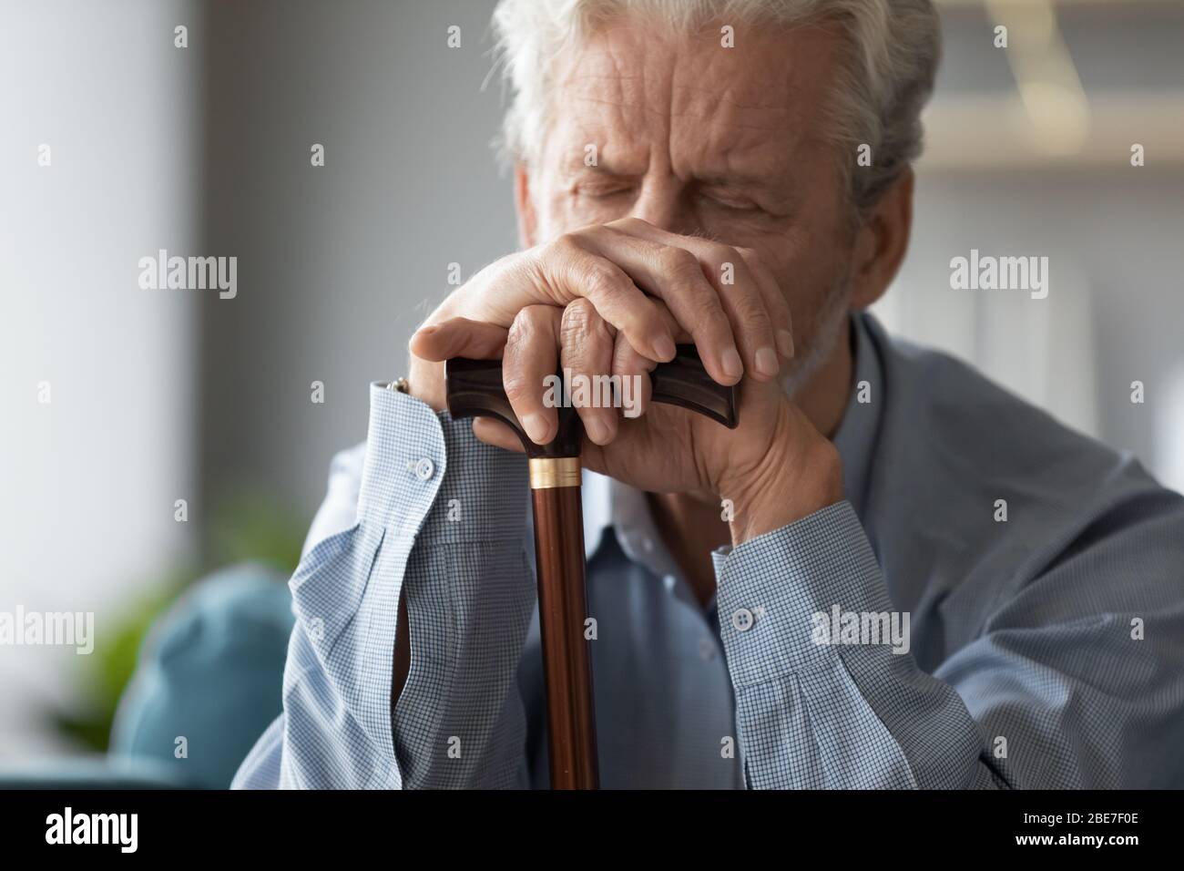 Nahaufnahme traurig älteren Mann, der die Hände auf Gehstock Stockfoto