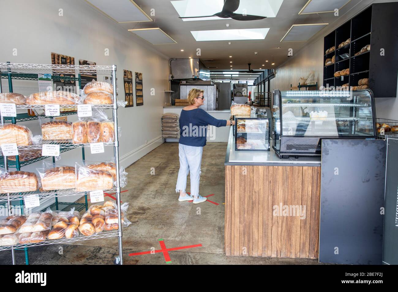 Frau Modell veröffentlicht kauft Brot in einer Bäckerei in Sydney, mit roten Kreuzen auf dem Boden, um soziale Distanzierung zu halten, Australien Stockfoto