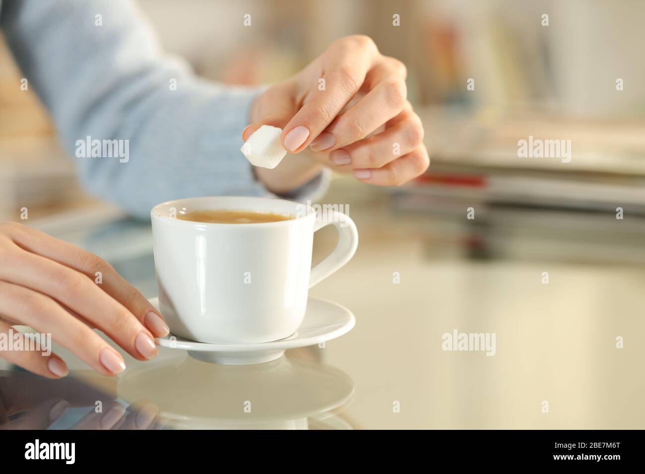 Nahaufnahme der Frau Hand hält Zucker Würfel über einer Kaffeetasse auf einem Schreibtisch zu Hause Stockfoto