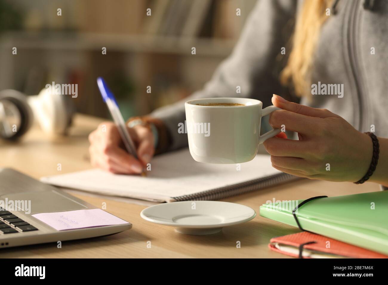 Nahaufnahme von Student Mädchen Hände Schreiben auf Notebook hält Kaffeetasse in der Nacht sitzen auf einem Schreibtisch zu Hause Stockfoto