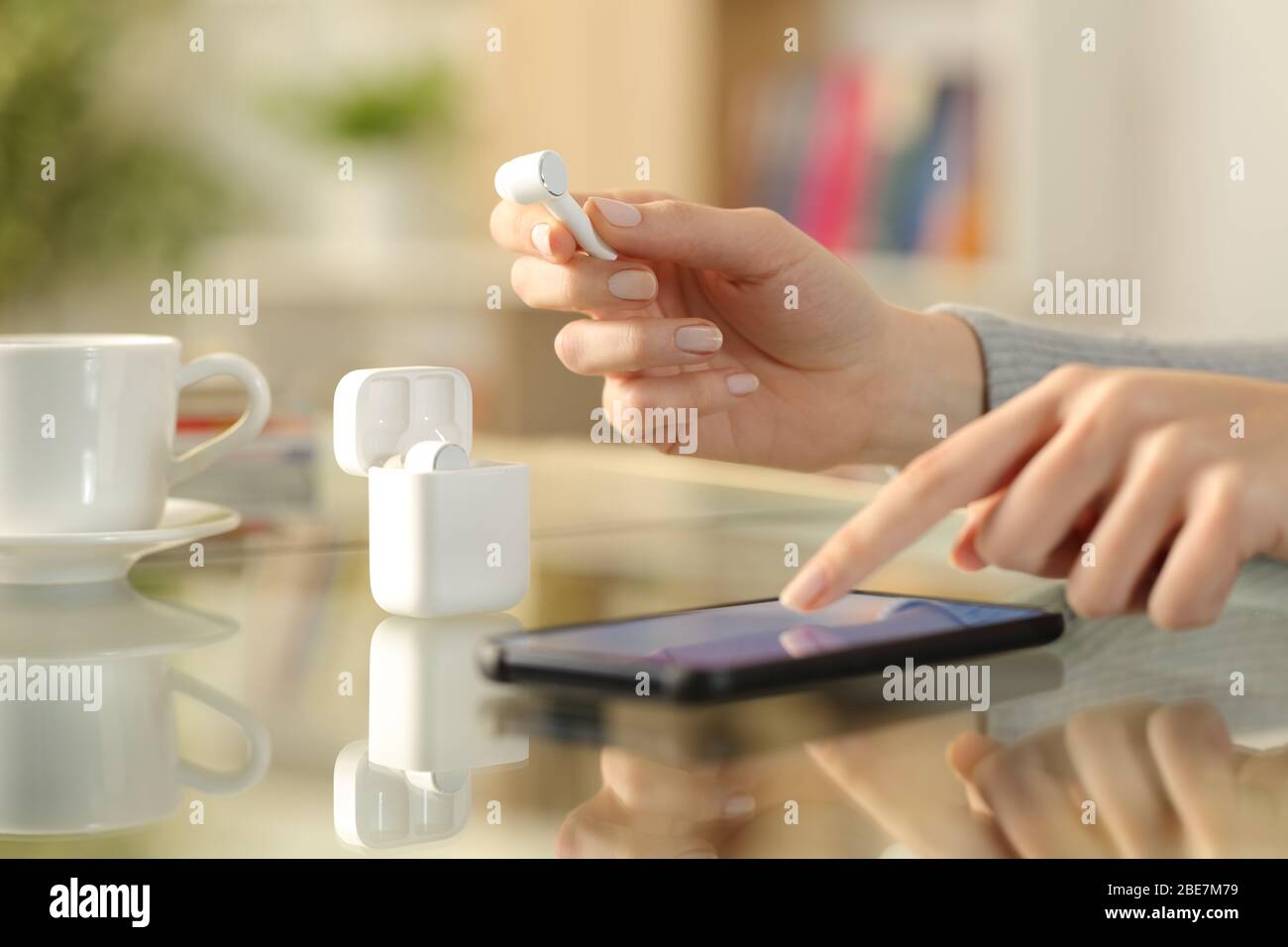 Nahaufnahme der Hände der Frau, die den Ohrstöpsel halten und das Smartphone auf einem Schreibtisch zu Hause überprüfen Stockfoto