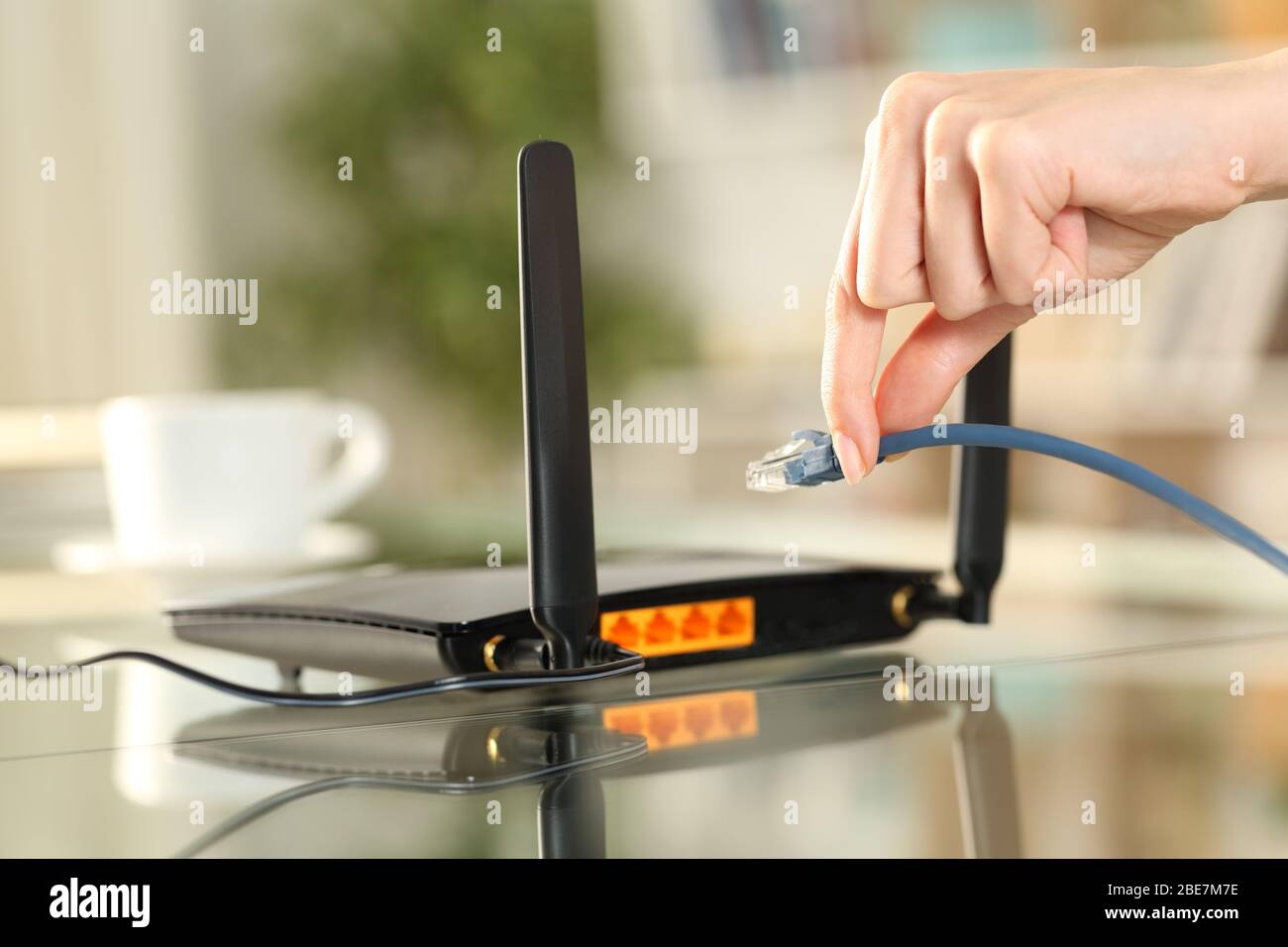 Nahaufnahme der Hände einer Frau, die das ethernet-Kabel an den Router auf einem Schreibtisch zu Hause anschließt Stockfoto
