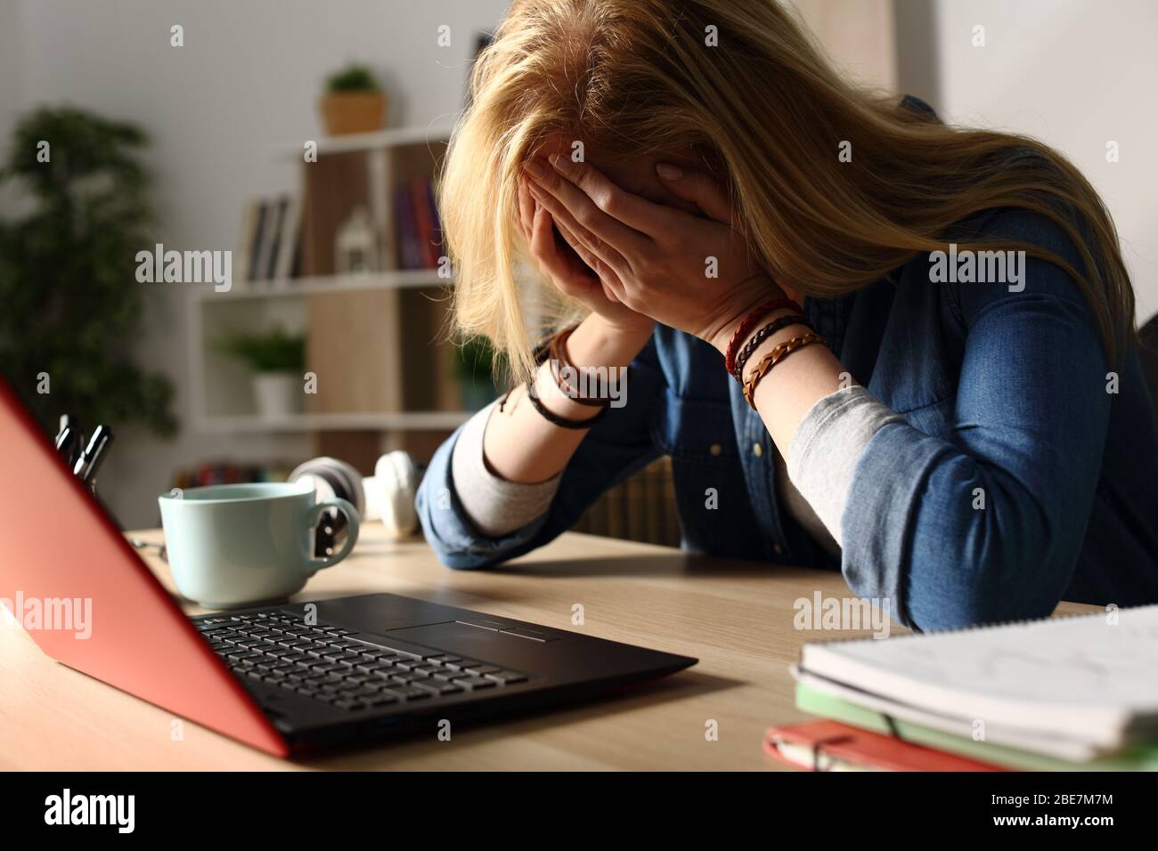 Nahaufnahme eines traurigen Studenten, der schlechte Nachrichten auf einem Laptop empfängt, der nachts auf einem Schreibtisch sitzt Stockfoto