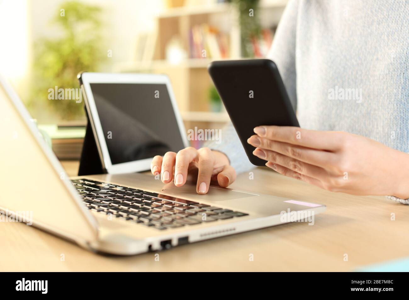 Nahaufnahme von Frauenhänden mit mehreren Geräten, die zu Hause auf einem Schreibtisch sitzen Stockfoto