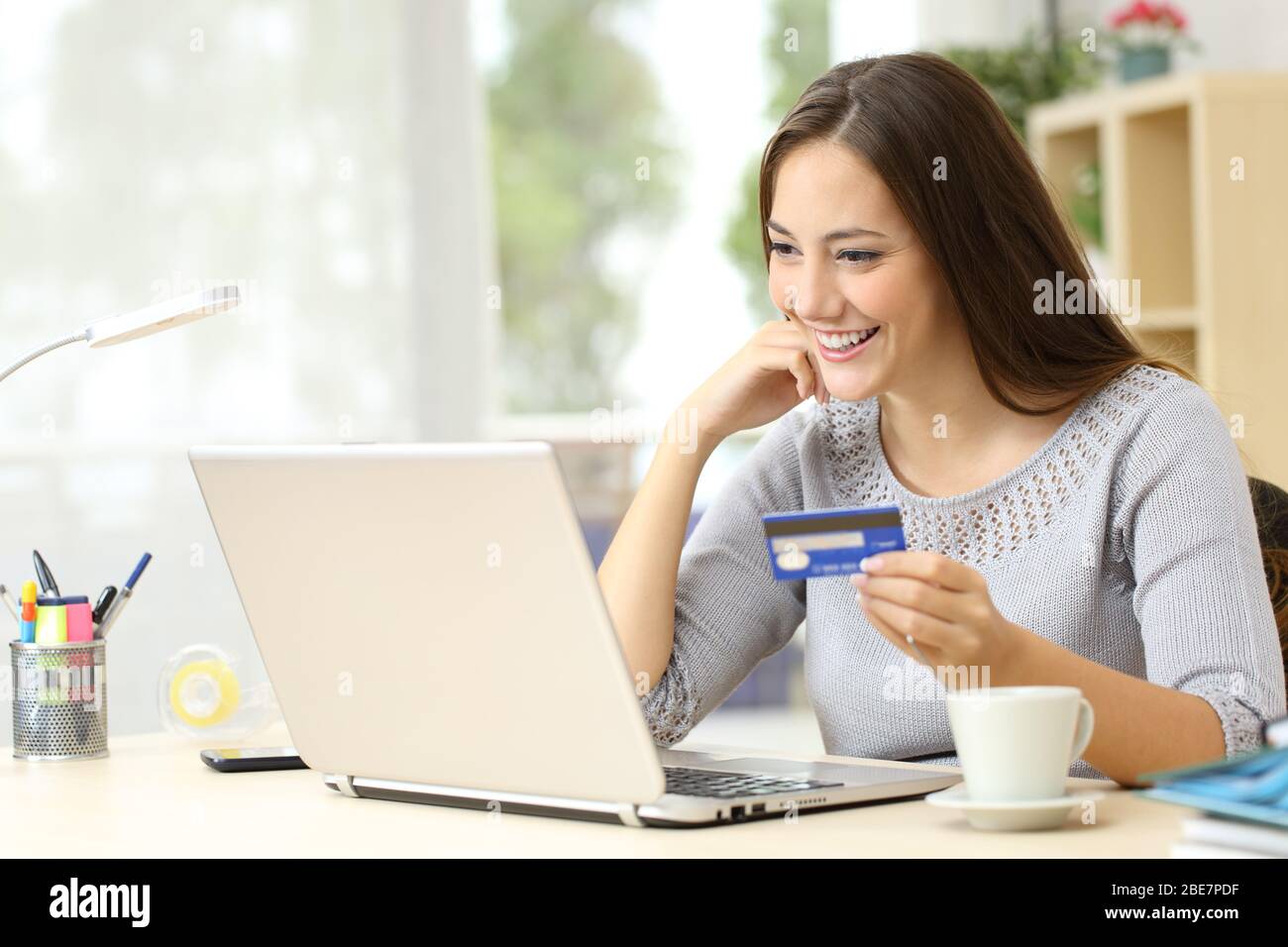 Glückliche Frau, die online mit Kreditkarte auf dem Laptop auf einem Schreibtisch zu Hause bezahlt Stockfoto