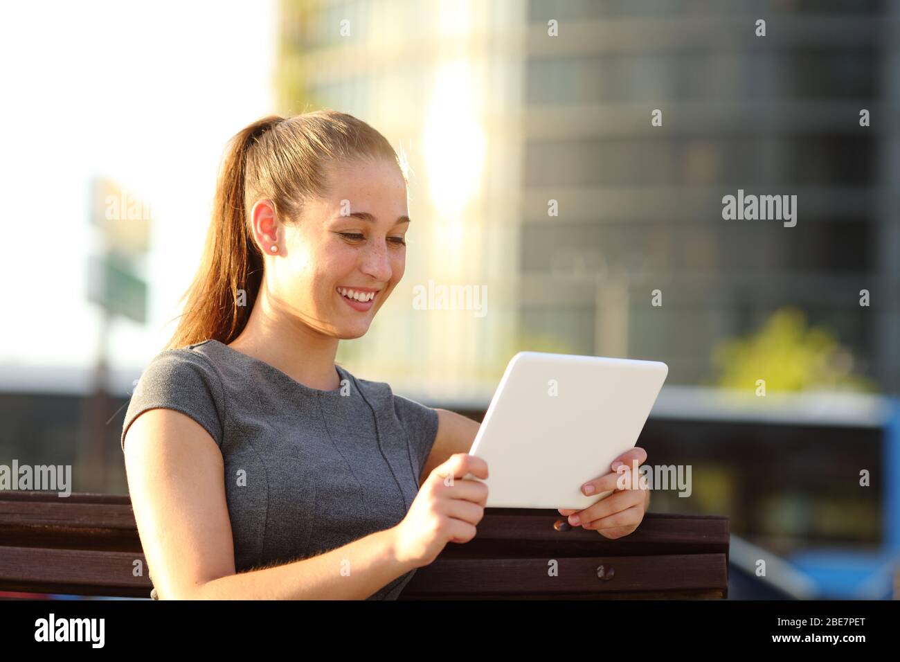 Glückliche Frau beim Ansehen von Videos online auf Tablet sitzen in einer Parkbank Stockfoto