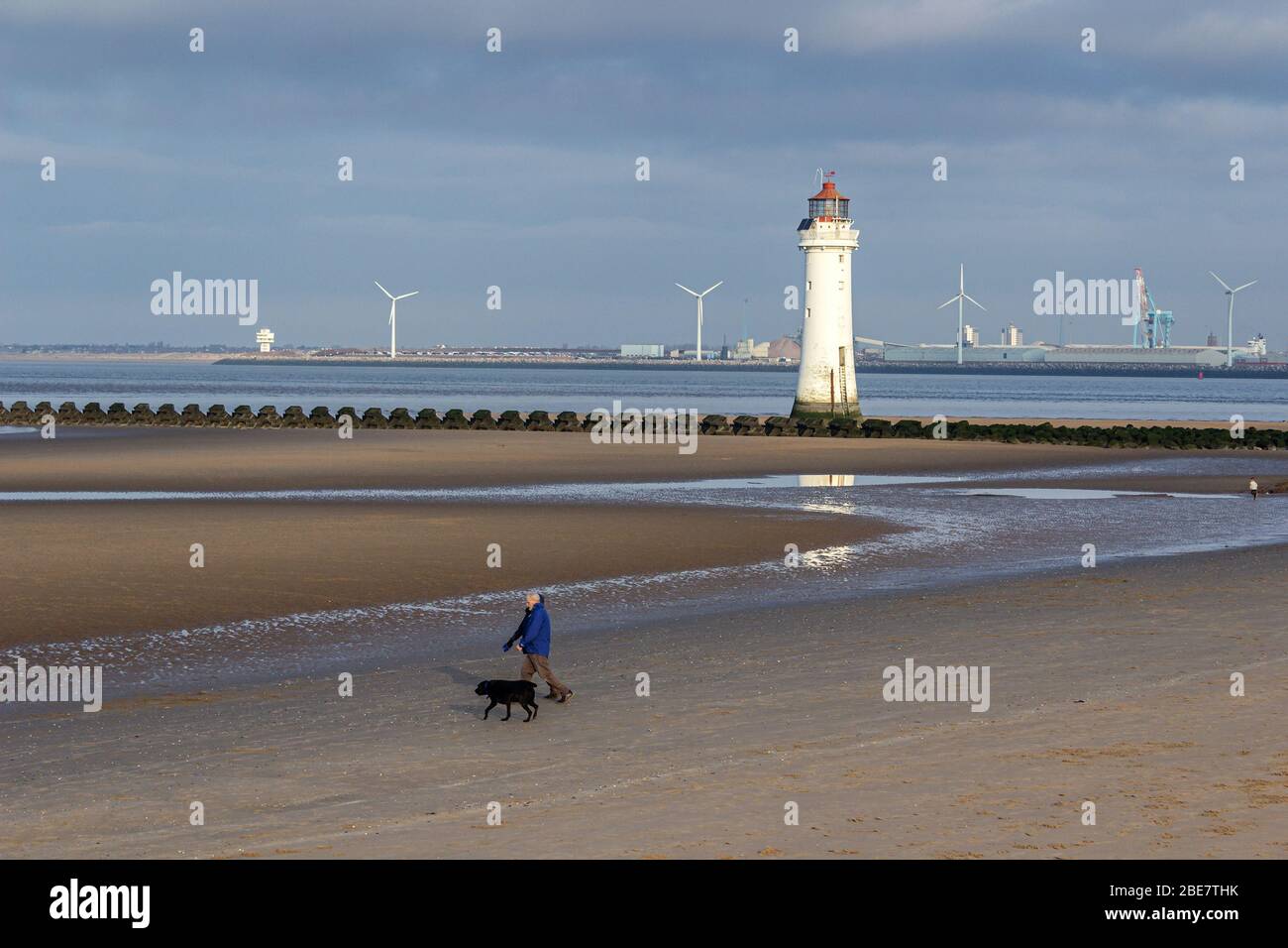 New Brighton Beach, Hundespaziergänger und Leuchtturm bei Ebbe. Liverpools Seaforth Docks im Hintergrund. Stockfoto