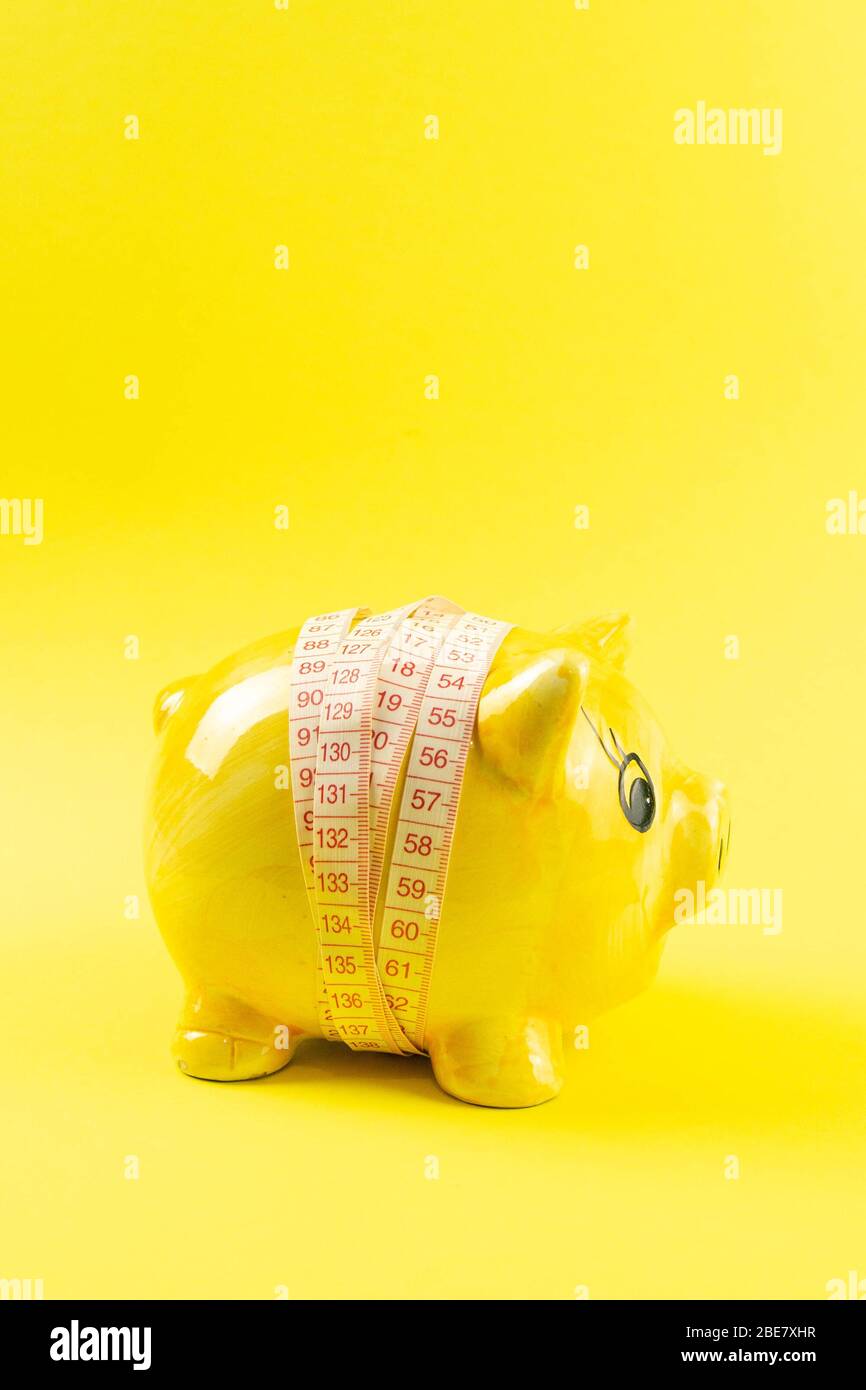 Gelbes Sparschwein in Form eines Schweins, das mit Maßband auf gelbem Hintergrund eingewickelt ist. Das Konzept der Geldeinsparung für den Gewichtsverlust Stockfoto