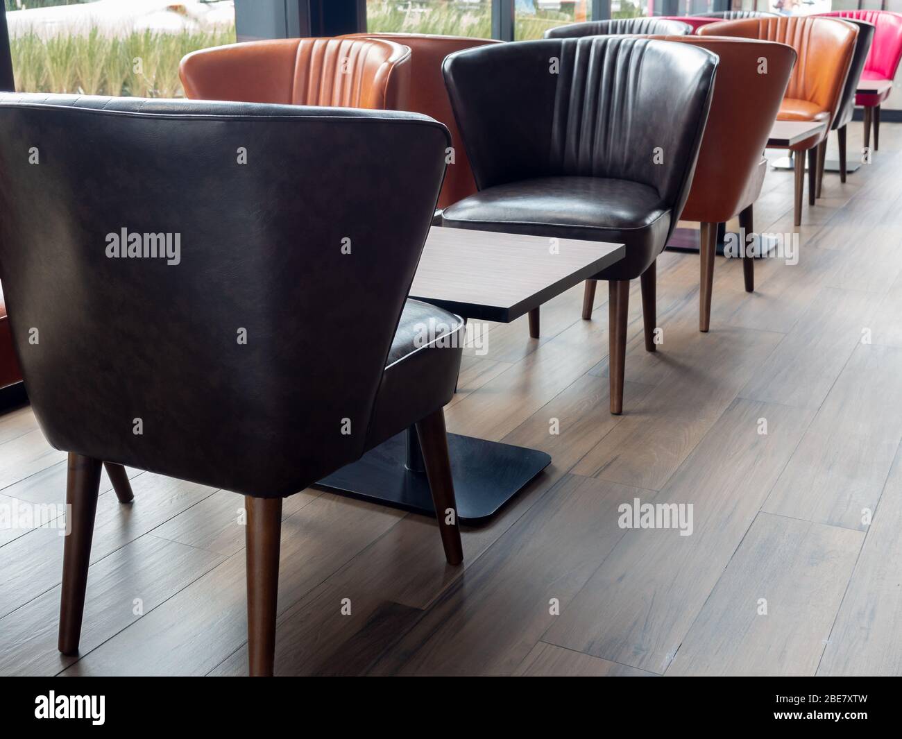 Lederstühle im Retro-Stil, orange und schwarze Farben und leerer Holztisch auf Holzfußboden im Café. Stockfoto