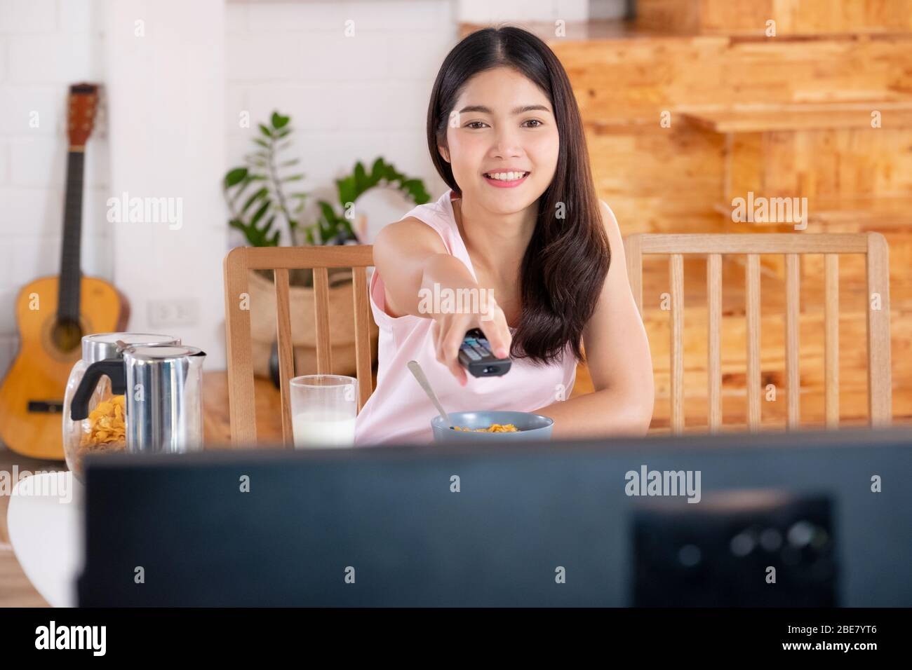 asiatische Frau watchcing tv auf Anfrage und verwenden Fernbedienung ändern Fernsehsender zum Frühstück am Morgen Stockfoto