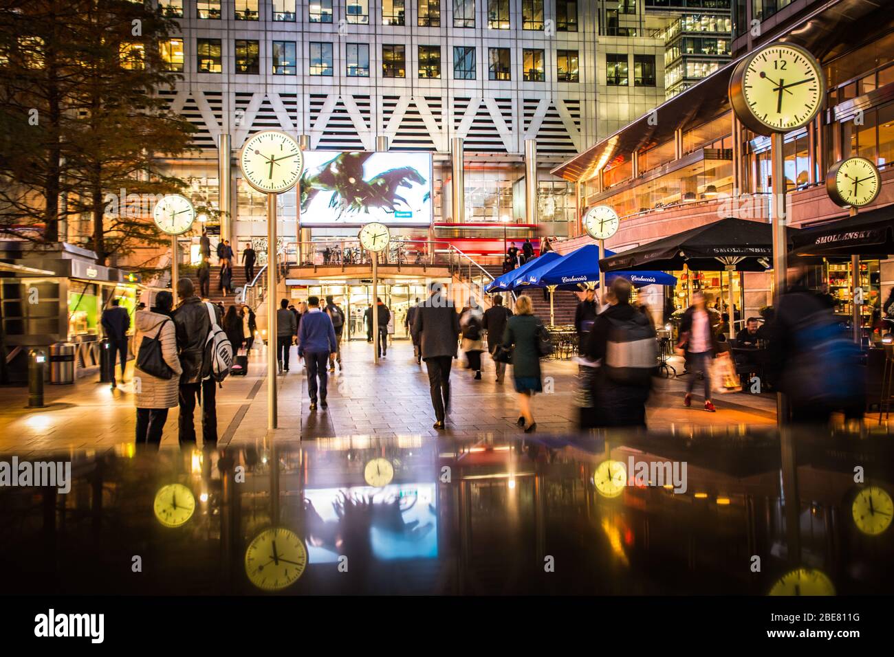LONDON - Geschäftsleute, die in Canary Wharf an der berühmten Uhr-Installation, Londons Finanzviertel, spazieren gehen Stockfoto