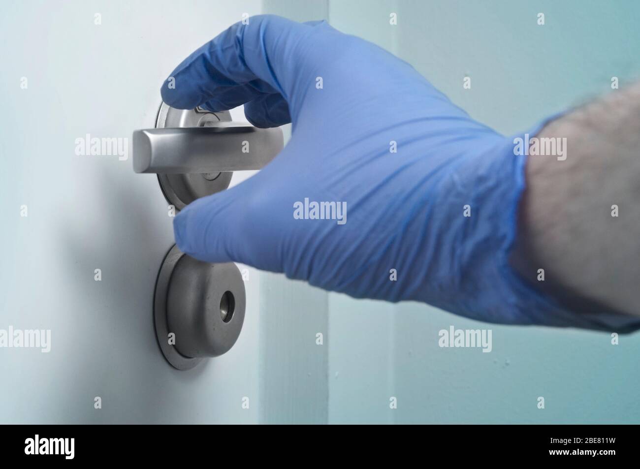 Hand in Einweg-Handschuh und Türgriff - Pandemien Vorsorge Stockfoto