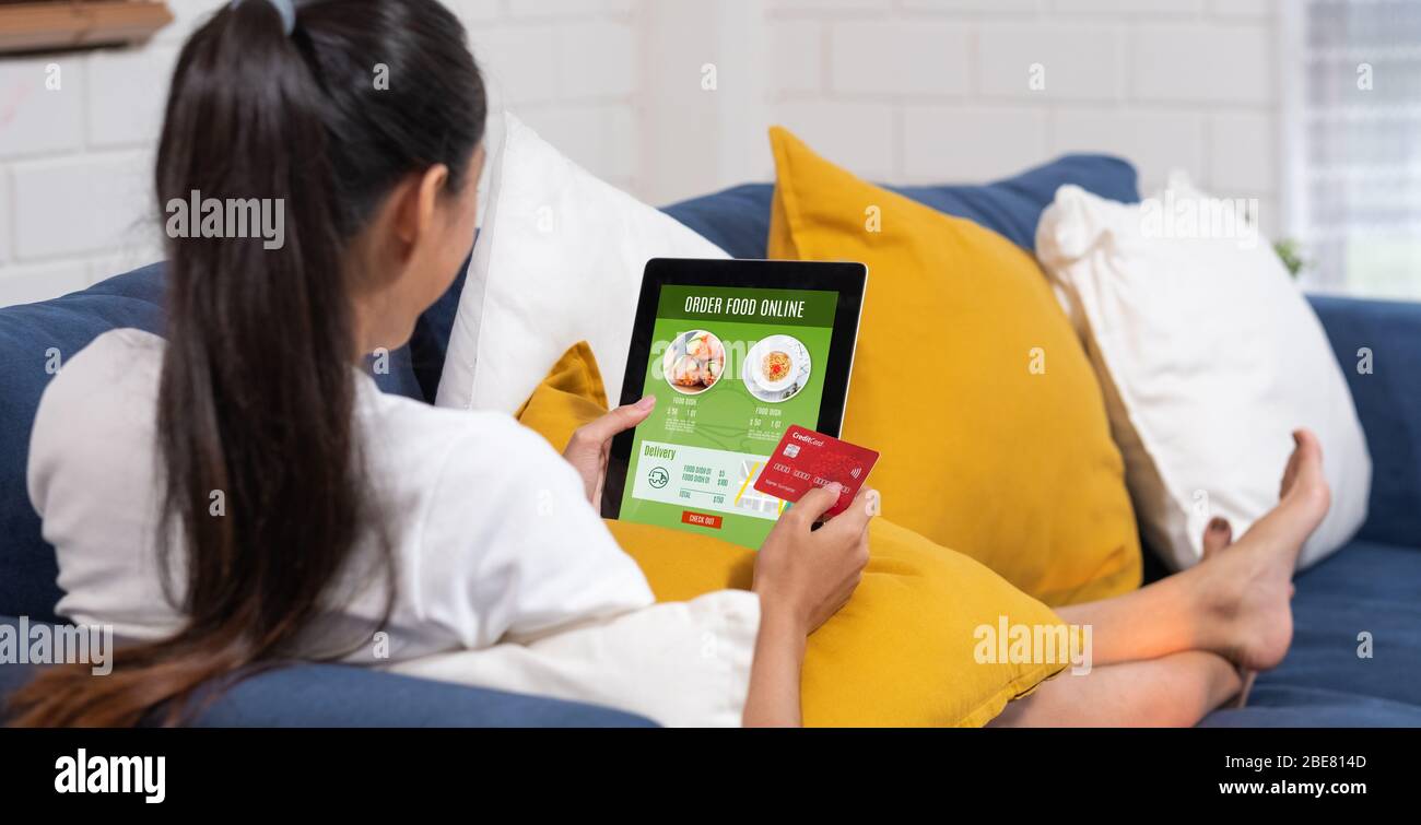 Asian Woman bestellt Lebensmittel online mit Kreditkarte auf Tablet auf dem Sofa zu Hause.digitaler Lifestyle mit Technologie Stockfoto
